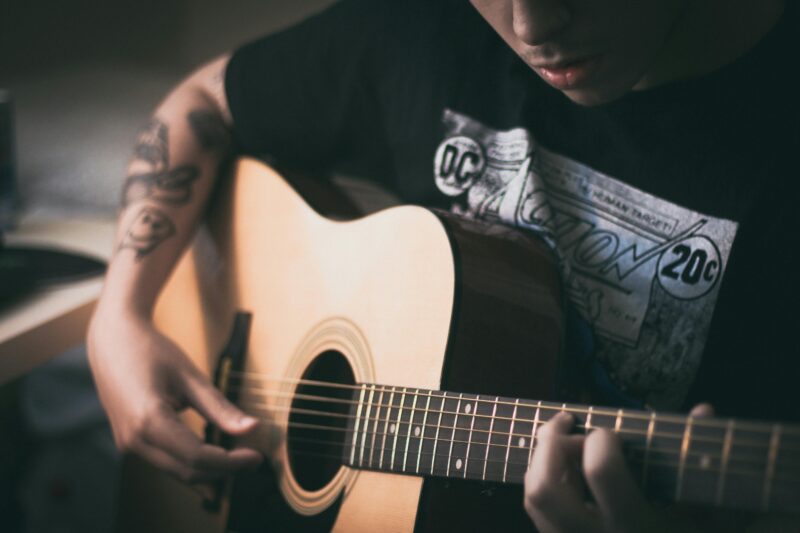 Close-up of a young tattooed musician playing an acoustic guitar indoors.