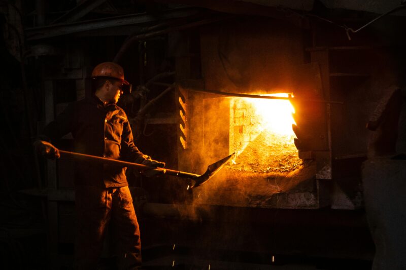 Blue-collar worker managing furnace in an industrial plant setting.