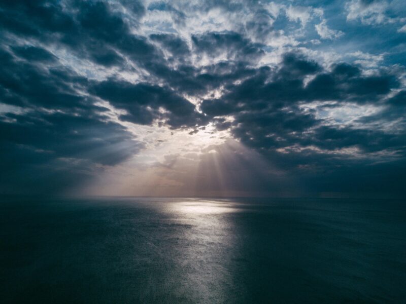 A breathtaking view of the ocean at sunset, with dramatic clouds and sunrays breaking through, creating a serene seascape.