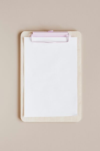 Top view of a minimalist wooden clipboard with blank paper against a neutral background.