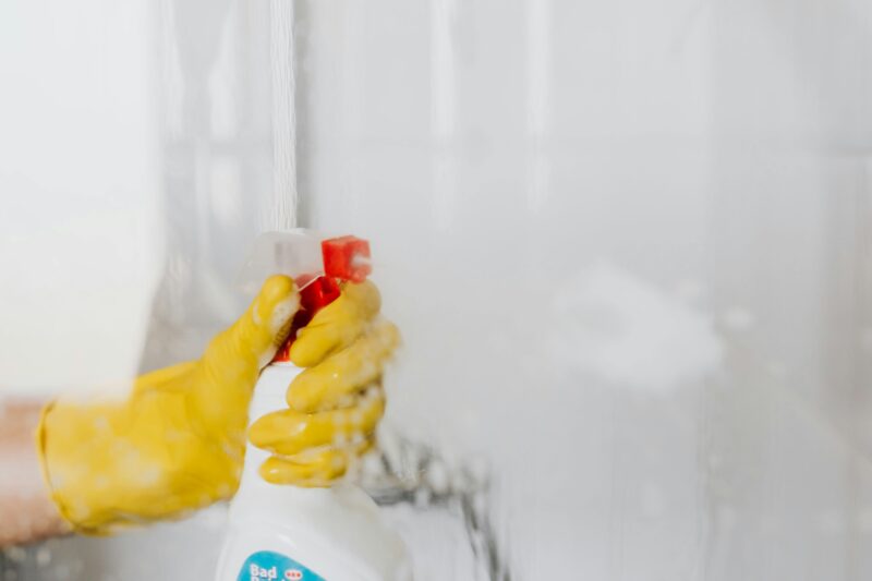 Person wearing yellow gloves cleaning a glass surface with a spray bottle.