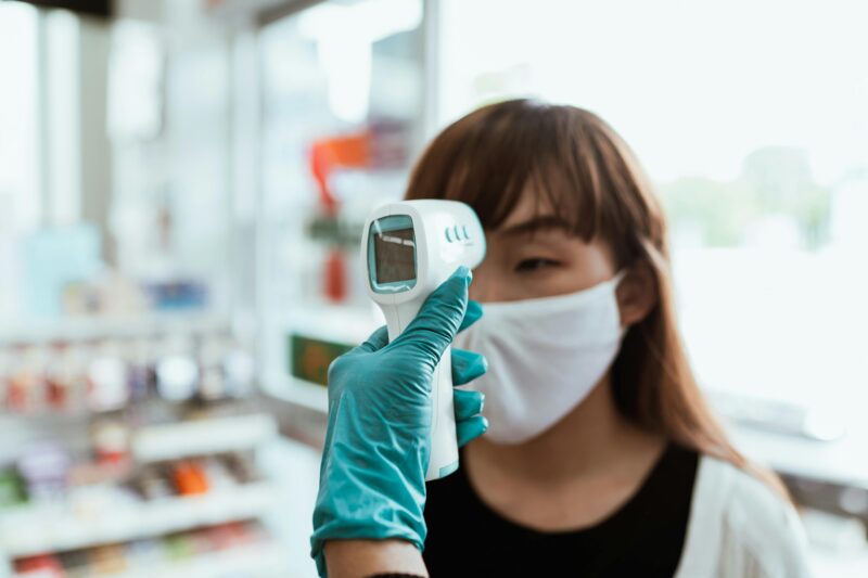 A woman in a face mask receives a contactless temperature check in a pharmacy setting.