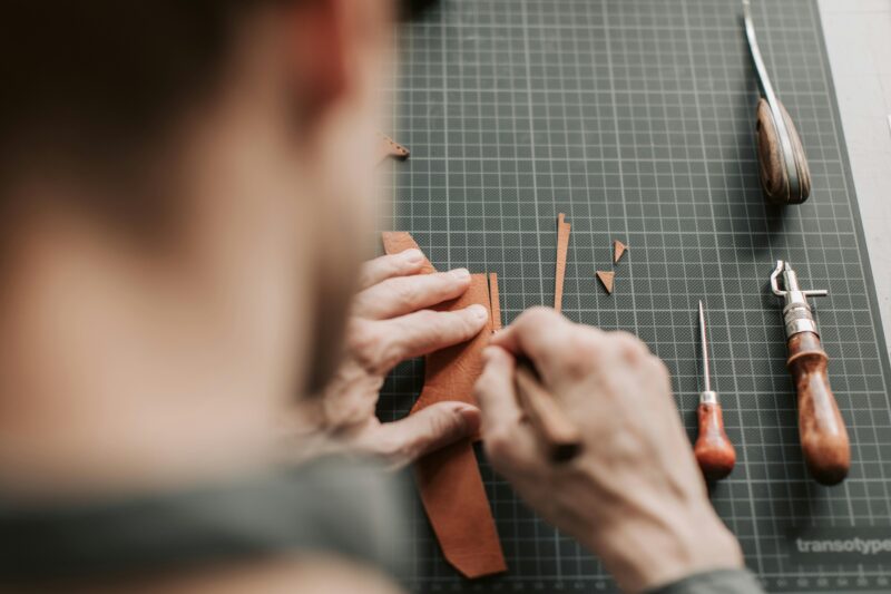 Close-up of a craftsman cutting leather with tools in a workshop setting.