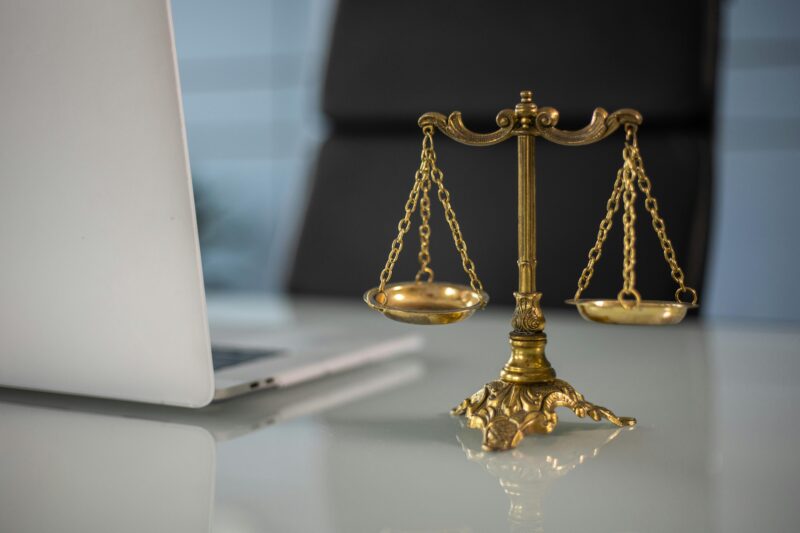 Golden justice scales on a desk beside a laptop, symbolizing law and balance.