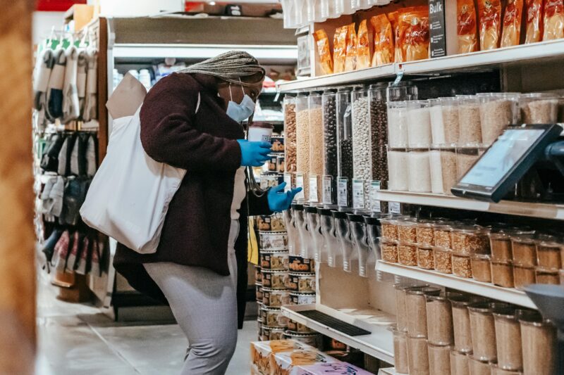 Plus size woman wearing mask and gloves selecting grains in a supermarket aisle.