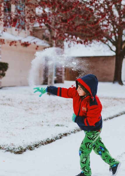 Young boy playing with snow in a suburban backyard, capturing a moment of winter fun.