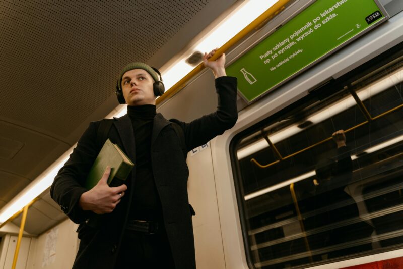 A man with headphones holds a book while standing in a subway car, urban journey captured.