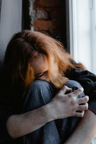 A woman showing signs of distress while seated indoors against a brick wall, holding her knees.