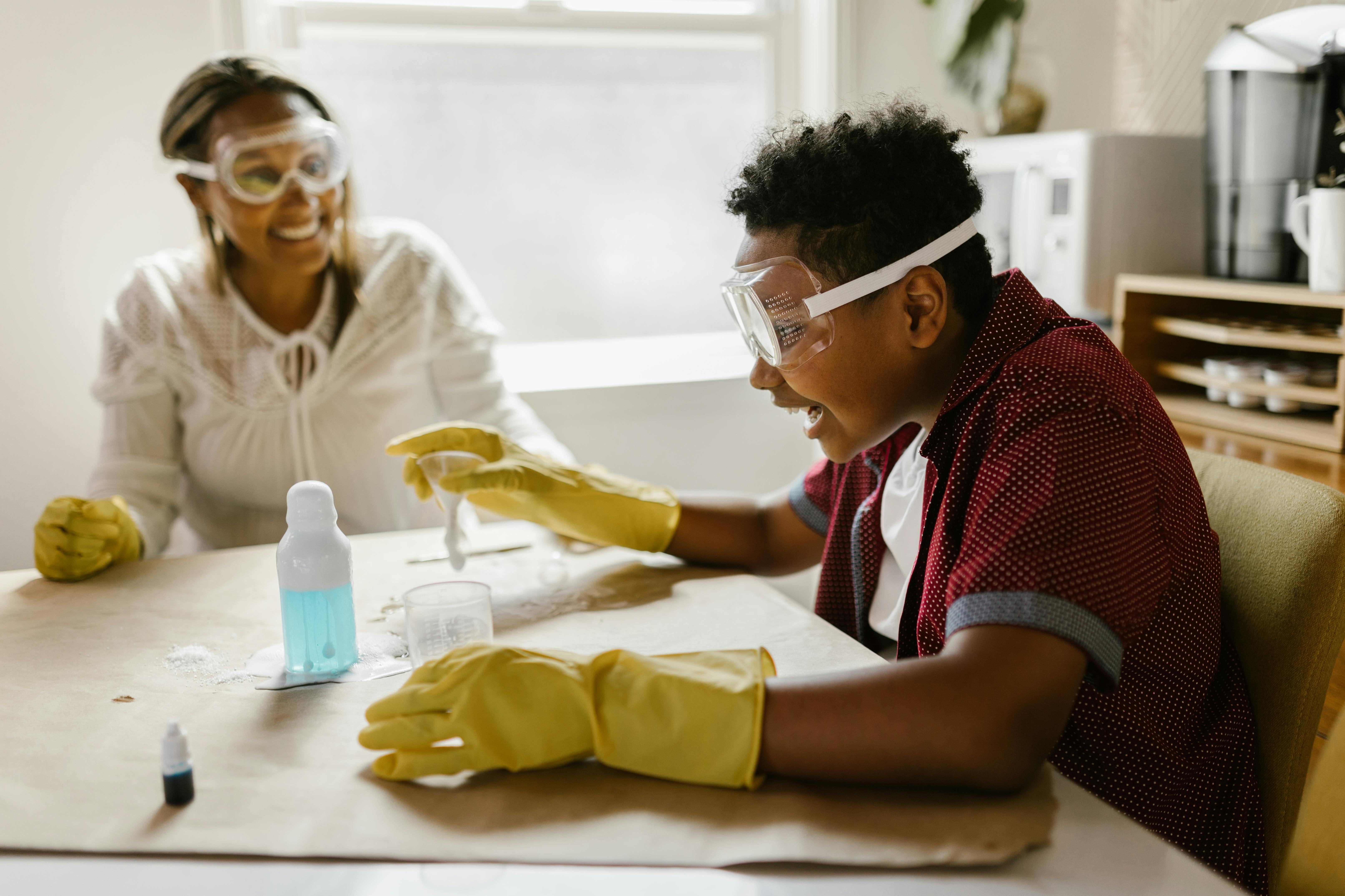 Boy and woman conducting a science experiment at home, wearing gloves and goggles.