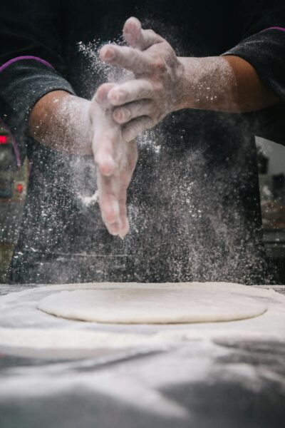 A chef clapping hands over dough, releasing flour in a kitchen setting.