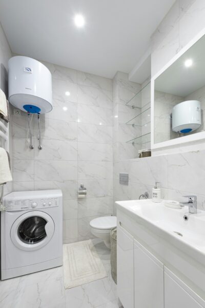 A sleek white bathroom featuring a washing machine, sink, and boiler.