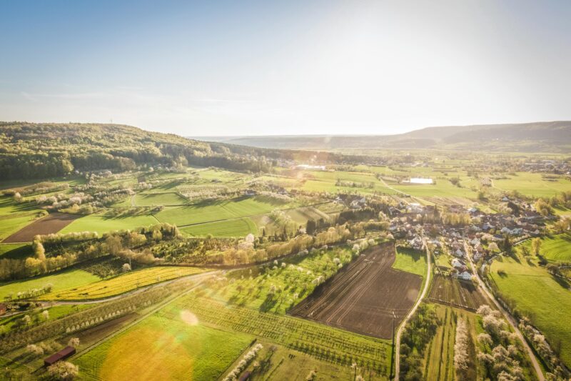 Scenic aerial view of a sunlit countryside village surrounded by green fields.