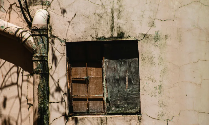 Close-up of an old building facade with a decaying window, emphasizing textures of aging and decay.