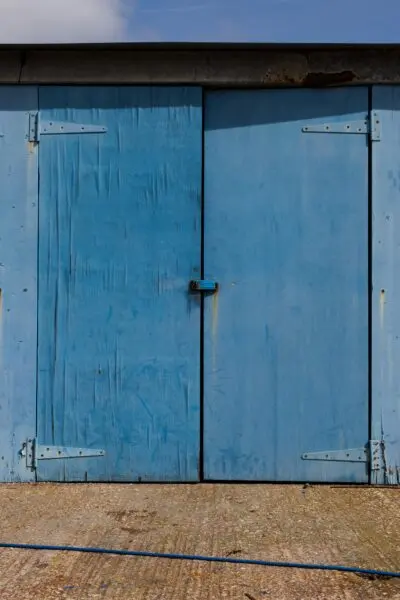 Rustic blue wooden garage door with metal hinges on barn exterior.