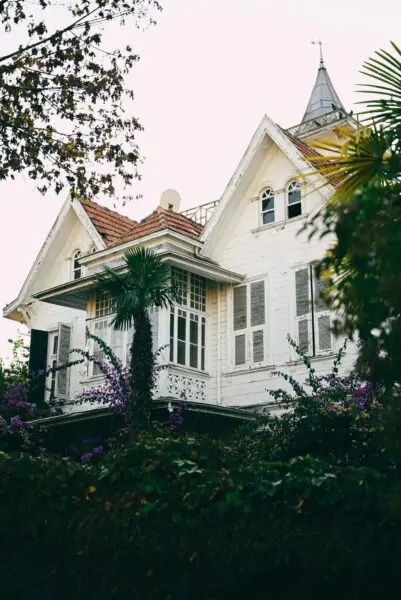 A beautiful white mansion surrounded by lush greenery with a turret roof.