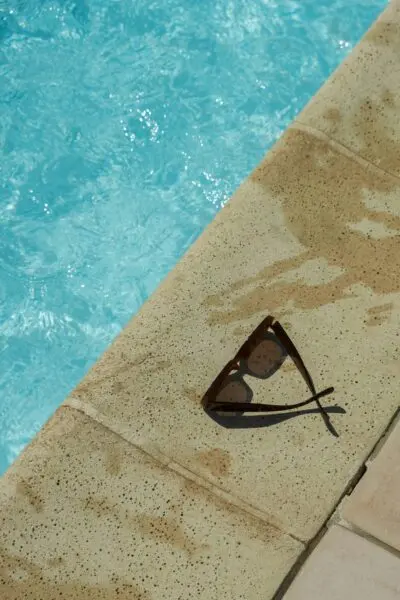 Close-up of sunglasses on a pool edge under the summer sun, capturing leisure and relaxation.