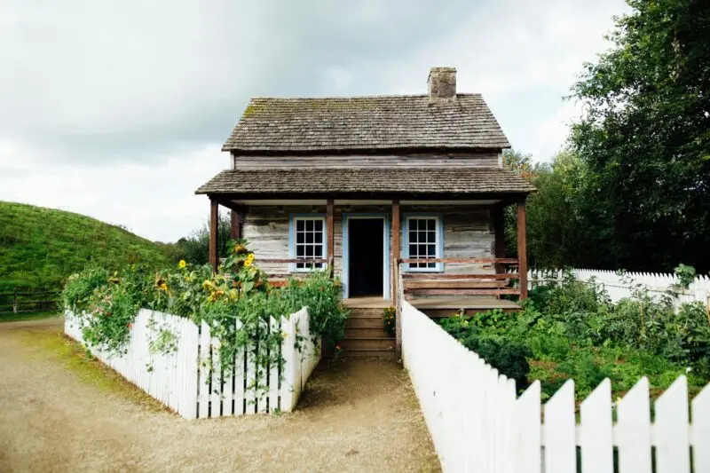 A quaint wooden cabin surrounded by greenery and a white picket fence