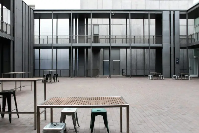 A contemporary patio space with tables and stools, surrounded by modern architecture.