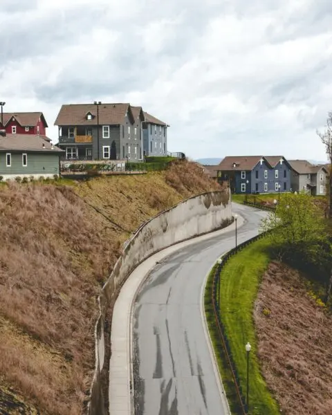 Aerial view of a curving road with hillside houses in Boone, NC, under a cloudy sky.