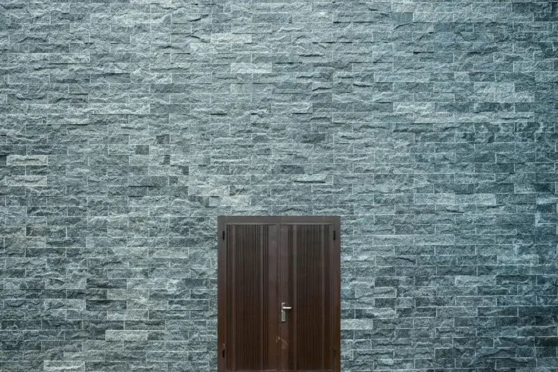 A minimalist stone brick wall featuring a simple wooden door, showcasing architectural design.