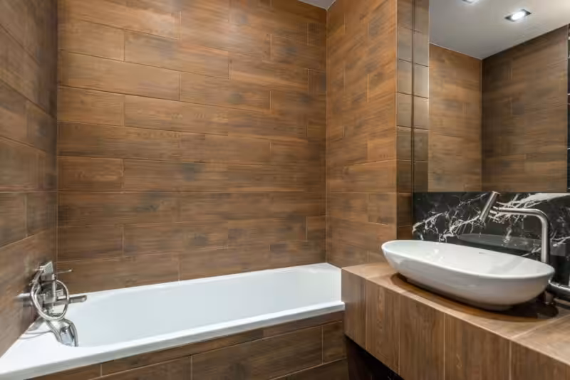 Modern bathroom interior with wood-look tile, white bathtub, sink, and faucet