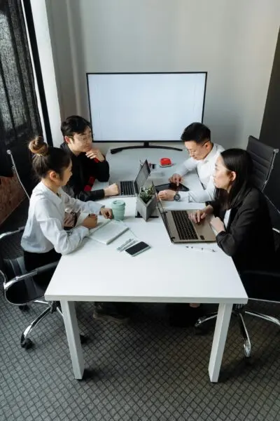 A group of professionals discussing a project in a modern office setting with laptops and a whiteboard.