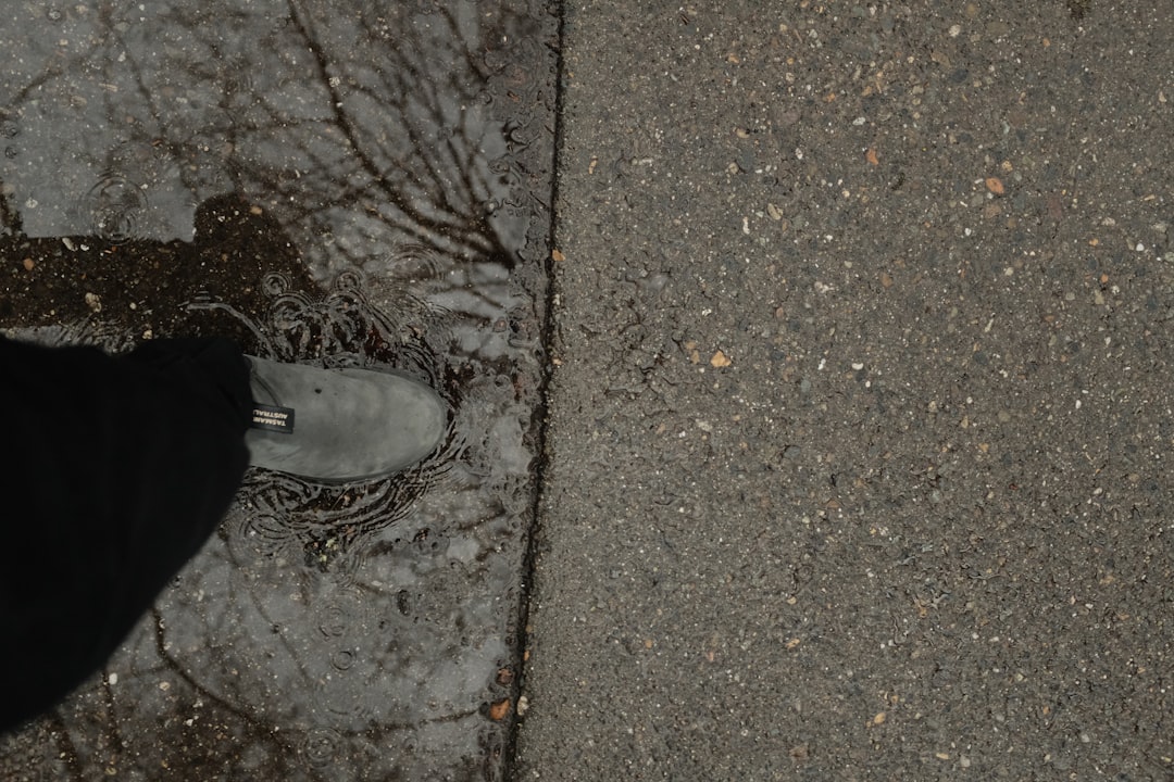 a person standing on a sidewalk next to a puddle of water
