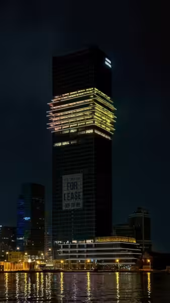 A night view of a towering skyscraper with colorful lights reflecting in the water in Ho Chi Minh City.