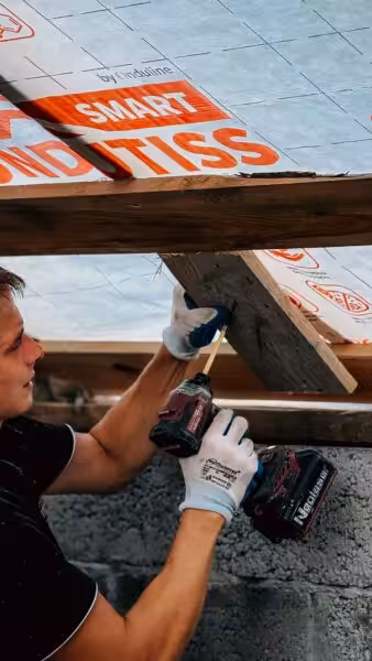 A construction worker uses a drill to install roof insulation, ensuring efficient energy management.