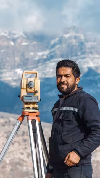 A surveyor operating a theodolite in a scenic mountain setting.