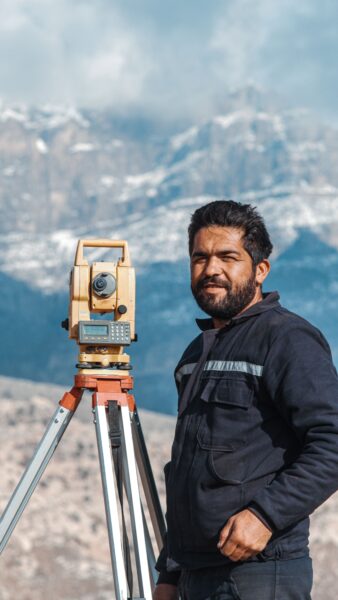 A surveyor operating a theodolite in a scenic mountain setting.