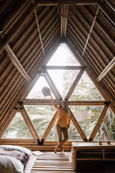 A woman in a bamboo house standing by a triangular window, enjoying the serene indoor ambiance.