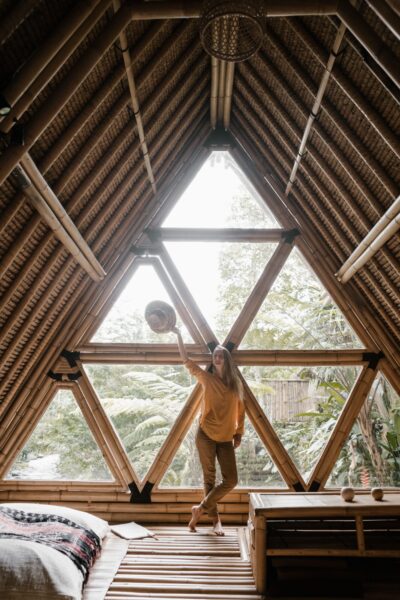 A woman in a bamboo house standing by a triangular window, enjoying the serene indoor ambiance.