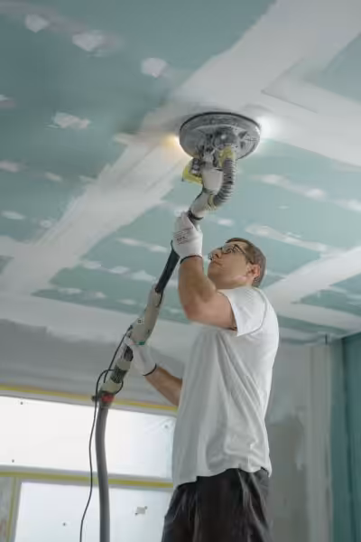 Adult male sanding a drywall ceiling with an industrial tool during home renovation.