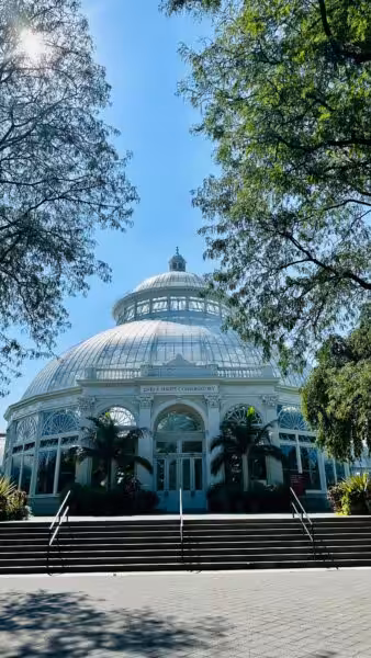 Captivating view of the Enid A. Haupt Conservatory on a sunny day framed by lush trees.