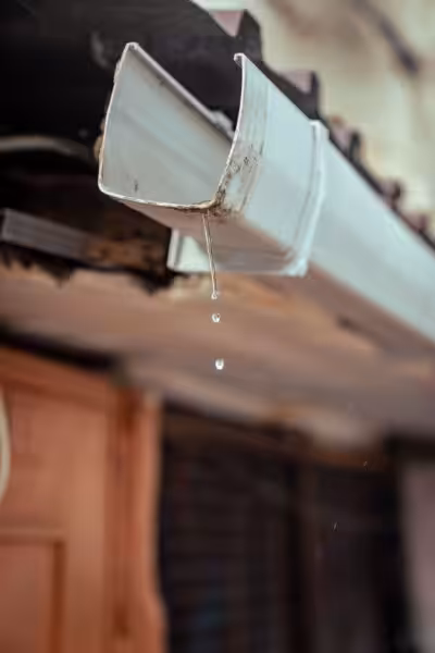 Detailed shot of rainwater droplets falling from a house gutter, emphasizing water flow.