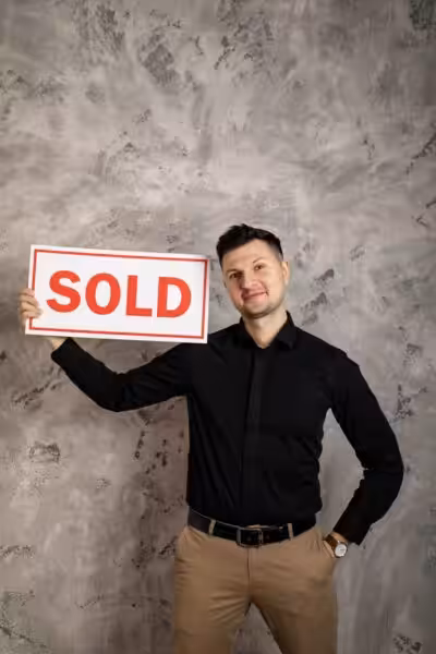 Smiling realtor holding a 'Sold' sign, symbolizing success in real estate transactions.