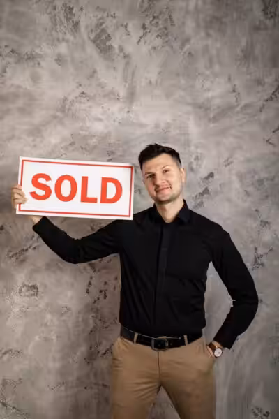 Smiling realtor holding a 'Sold' sign, symbolizing success in real estate transactions.