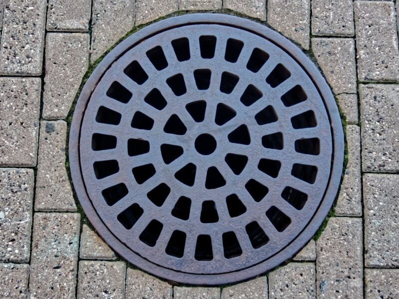 A metal storm drain cover in stone pavement.