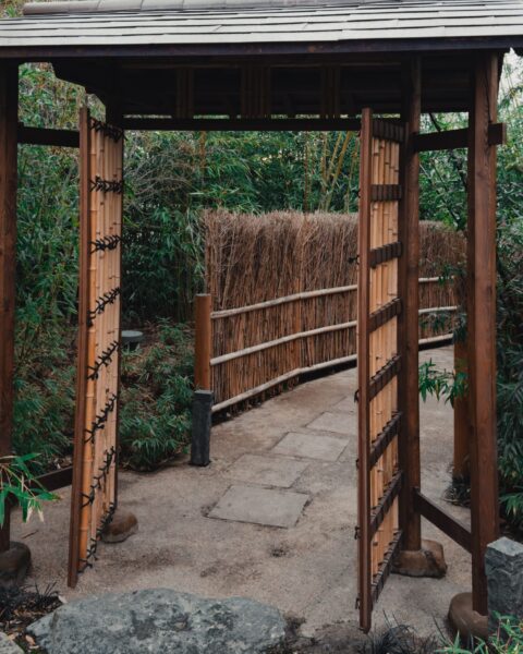 A tranquil bamboo gate surrounded by lush greenery and stone path.