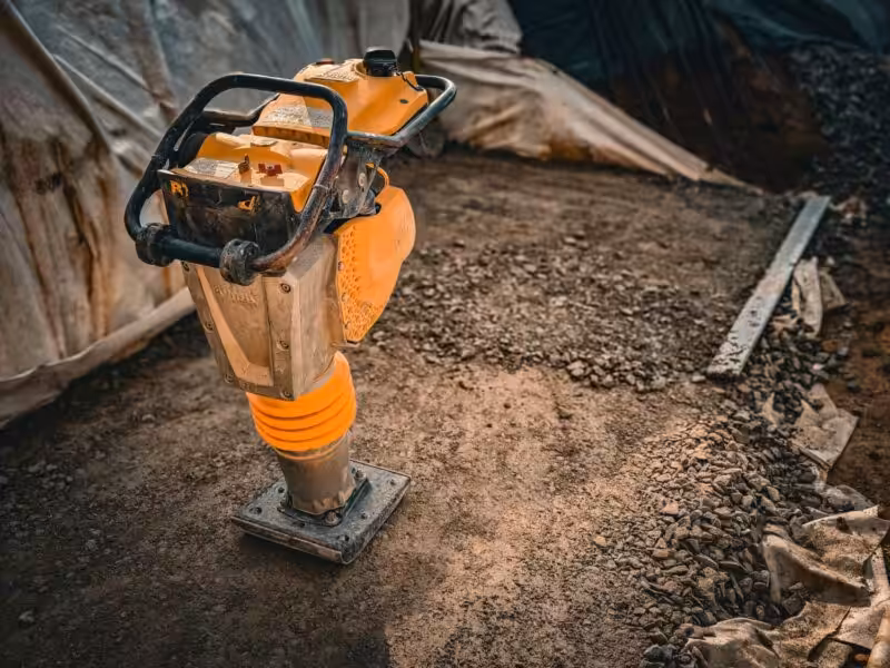 Close-up of a vibratory compactor on a construction site with gravel and soil.