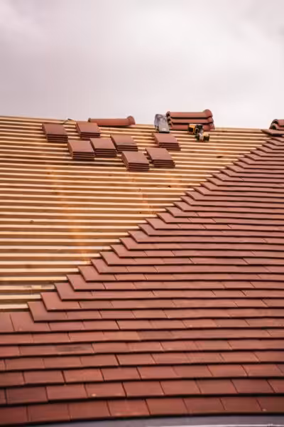 Partial installation of a terracotta tile roof on a building in progress.