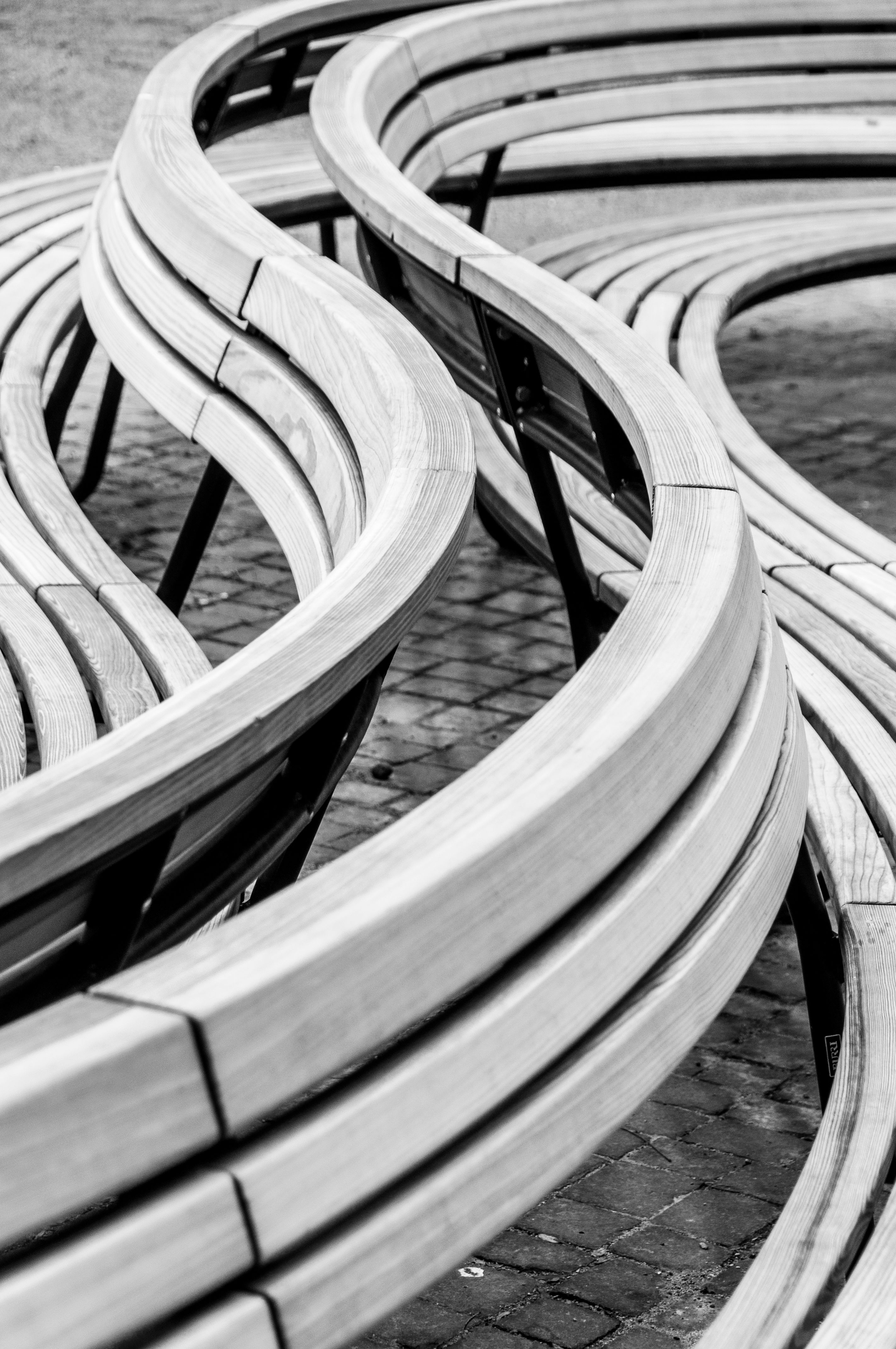 Abstract black and white photo of modern curved wooden benches on cobblestone pavement.