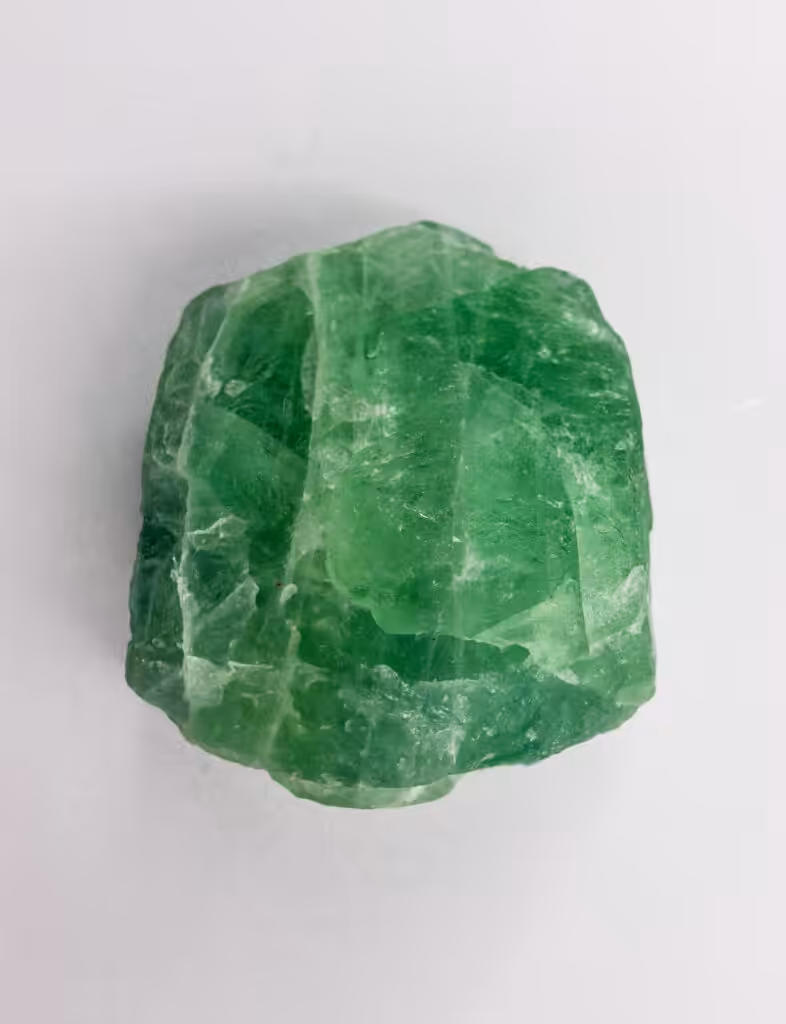 A striking green emerald gemstone with a rough texture on a light background, perfect for jewelry designs.