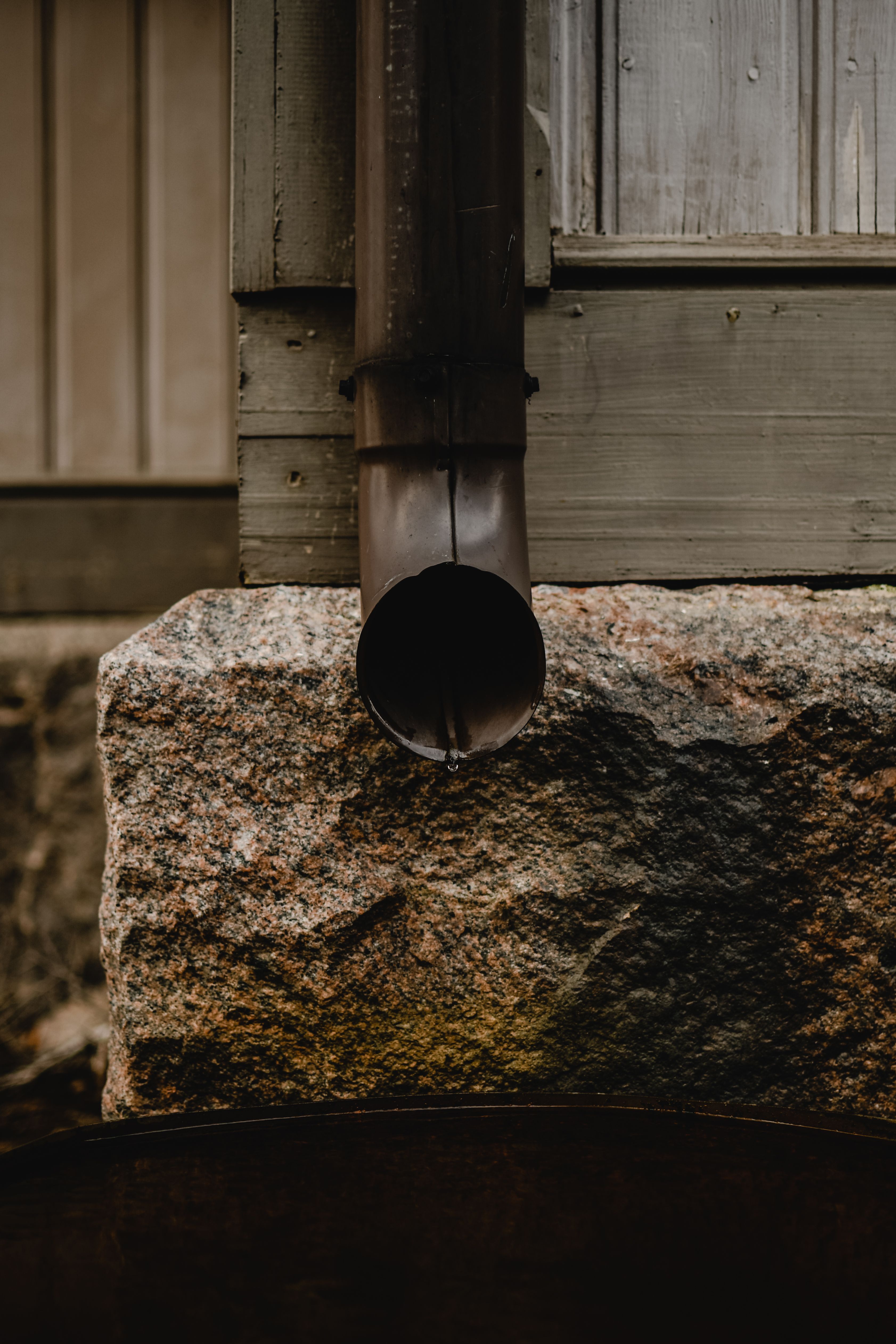 Rustic downspout with a drip on a stone wall in Helsinki, Finland.