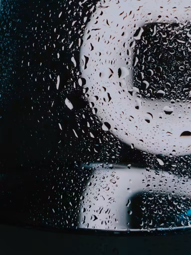 Through wet glass with water drops of white illuminated signboard on rainy night