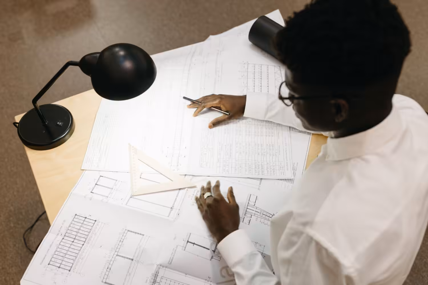 Top view of architect with afro hair working on blueprints at desk inside an office.