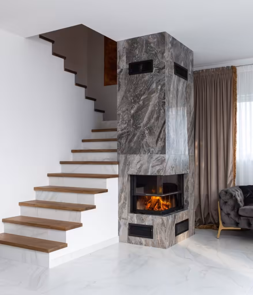 Interior of stylish living room with white stairway and wooden steps placed near marble column with burning fireplace.