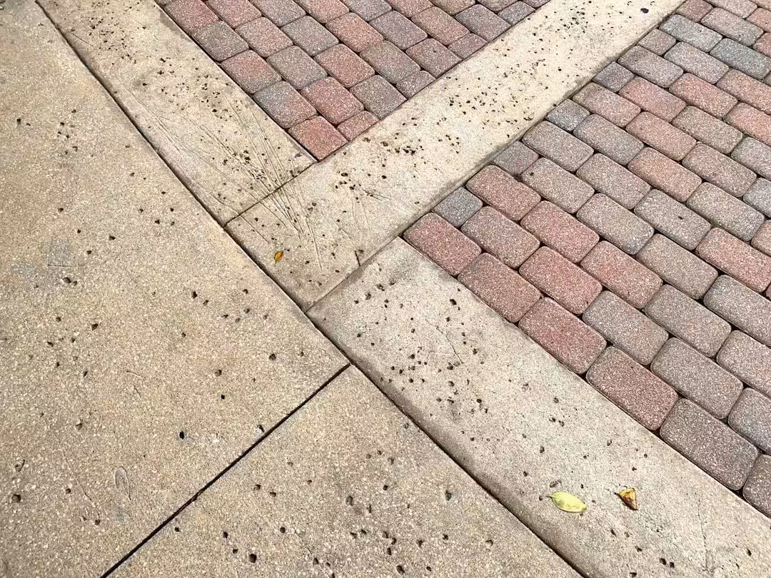 A sidewalk and parking lot create an interesting geometric abstract from the red bricks and concrete.