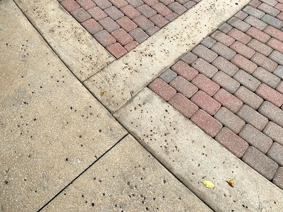 A sidewalk and parking lot create an interesting geometric abstract from the red bricks and concrete.
